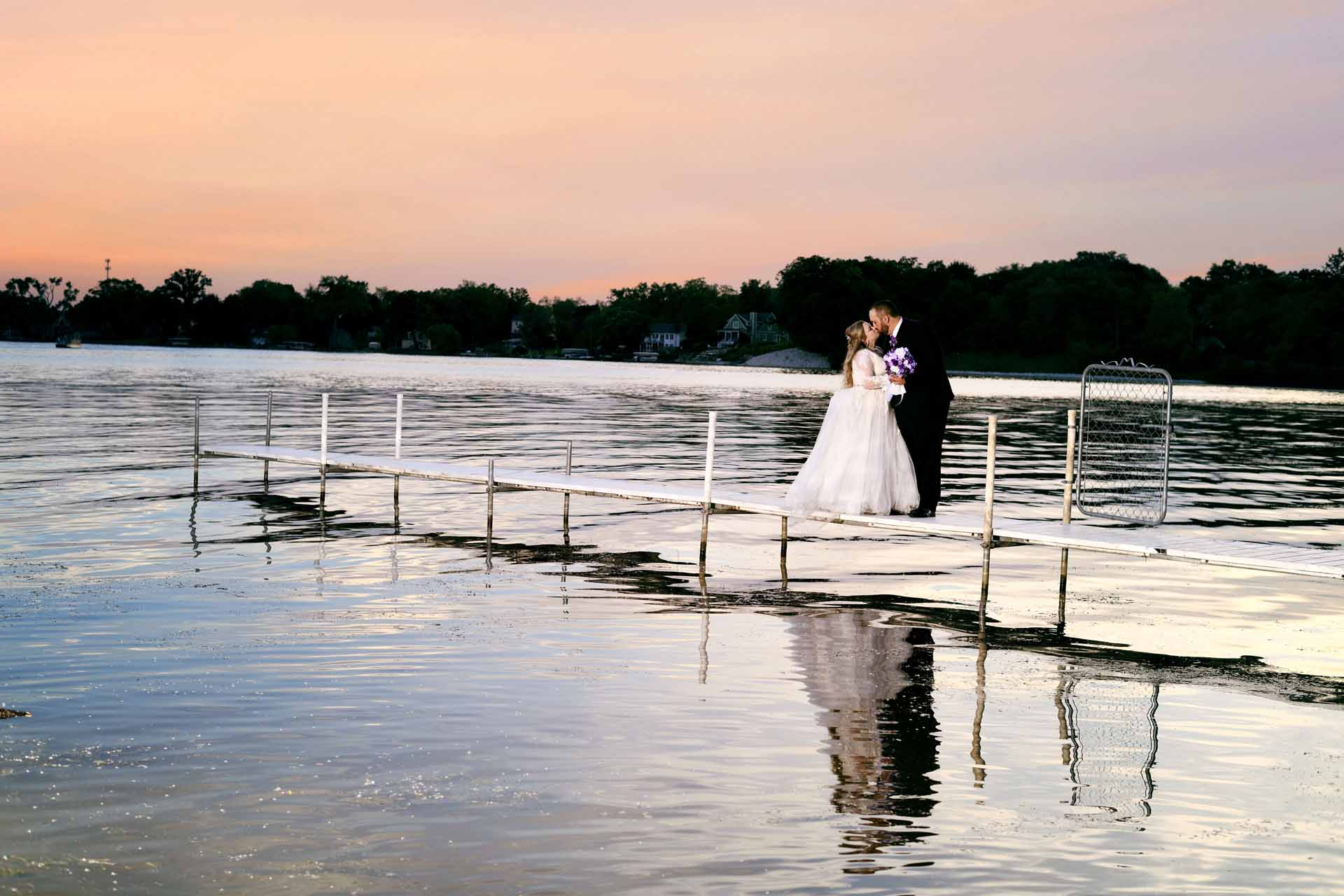 Bride and groom embracing on lakeside pier.